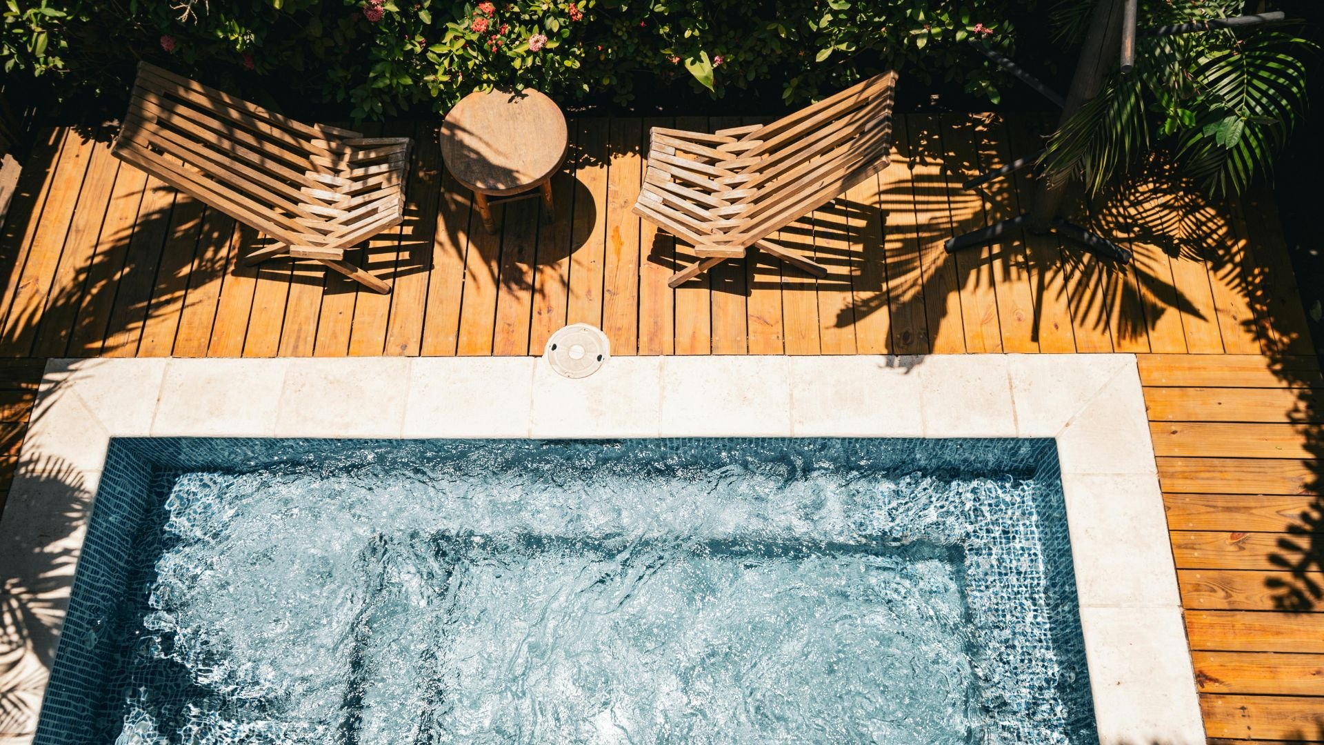 Luxurious wooden deck with jacuzzi, lounge chairs, and tropical plants