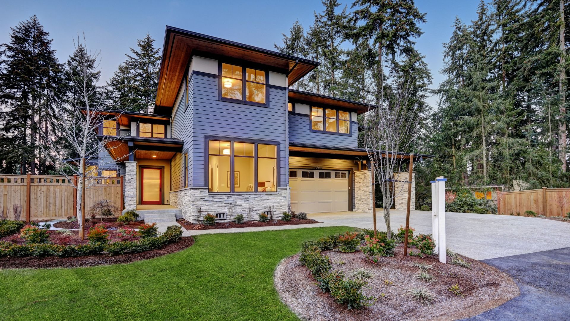 Modern two-story house with blue siding, warm windows, and landscaped yard