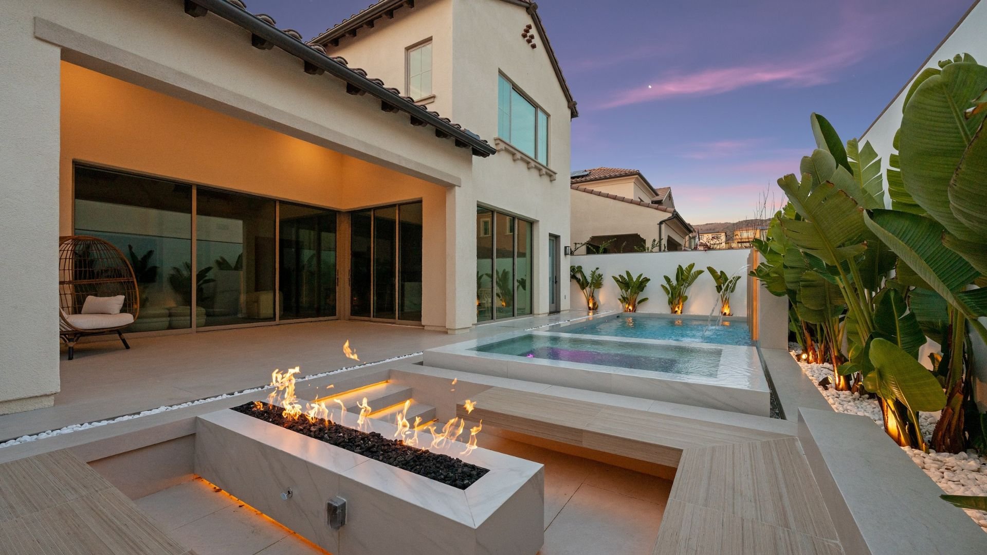 Luxury backyard with swimming pool, fire pit, and modern house at sunset